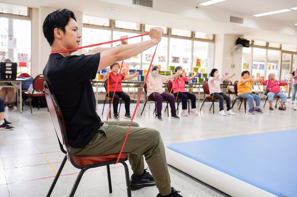 擁有晚美人生 板橋健華新城社區照顧關懷據動靜皆宜 1 《圖說》專業健身教練史提夫在健華新城社區照顧關懷據點帶領長輩使用彈力帶運動。〈社會局提供〉