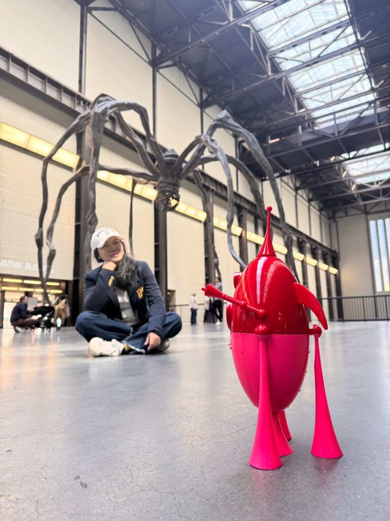 藝術家廖迎晰帶著粉紅雕塑〈重返地球〉到倫敦泰德美術館，並在路易斯作品前打卡。圖